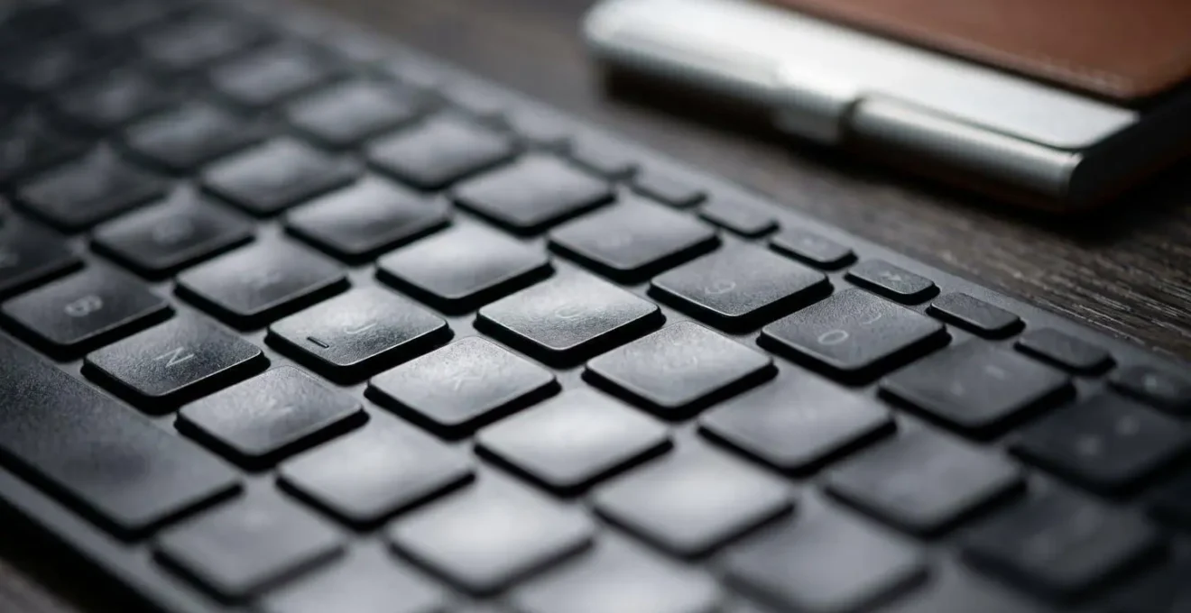A macro shot of a modern laptop keyboard, with textures and light creating an abstract professional aesthetic, a business card holder blurred in the background.